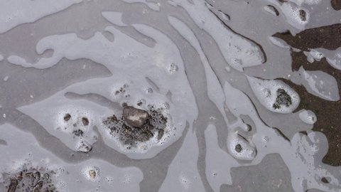 Close up liquid waste from detergent soap with white foam mixed with the rest of the washing and laundry water on soil floor which causes environmental pollution from household and industrials. 