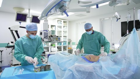 KYIV, UKRAINE - May 2021: Surgeon and assistant are performing surgery on belly. Liposuction process in hospital operating room. Plastic surgery for pumping fat. Healthcare.