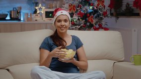 POV of woman using video call communication and eating chips. Festive adult talking to family on online remote conference for christmas eve festivity. Cheerful person looking at camera