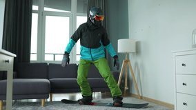 Funny video. Man dressed as a snowboarder depicts snowboarding on a carpet in a cozy room. Waiting for a snowy winter. Slow motion