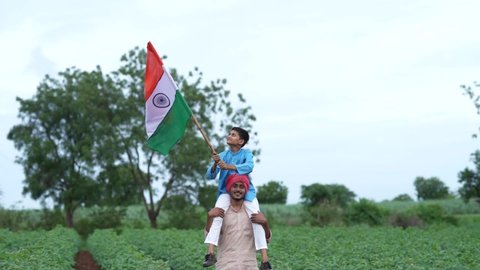 young indian farmer and his child waving national tricolor flag at agriculture field.