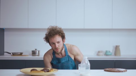 Masturbation concept. Glaze preparation. Whipped cream. Young handsome curly guy cooking in kitchen. He is wearing a blue apron. High quality 4k footage.