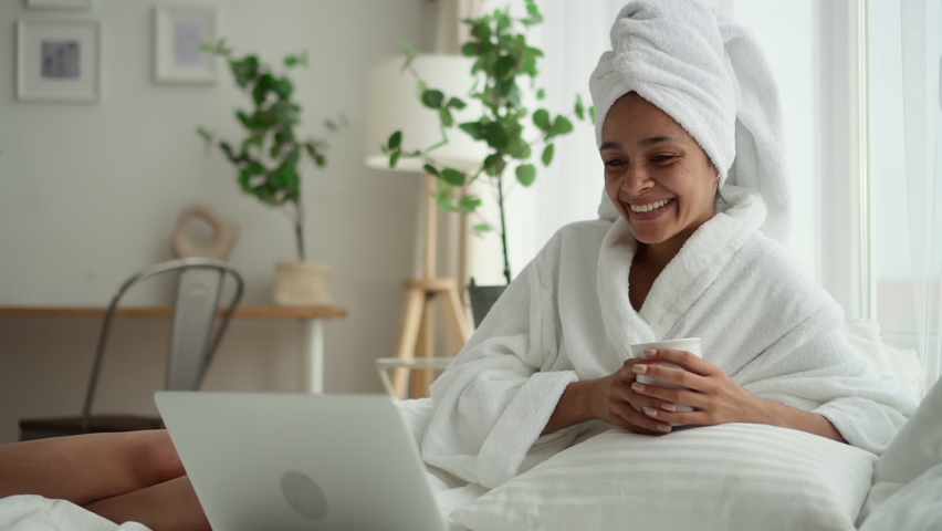 Beauty body care and online chat. Spbd Pretty black woman in terry bathrobe nods head with surprise talking to friend at videocall via laptop in bed at home Royalty-Free Stock Footage #1079116919