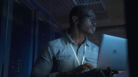 IT specialist using laptop and checking networks during working hours in render farm spbas. Close-up view of American African man holds computer in hand and does analytical job, inspects equipment or - Powered by Shutterstock - Get 15% off with code: PIKWIZARD15