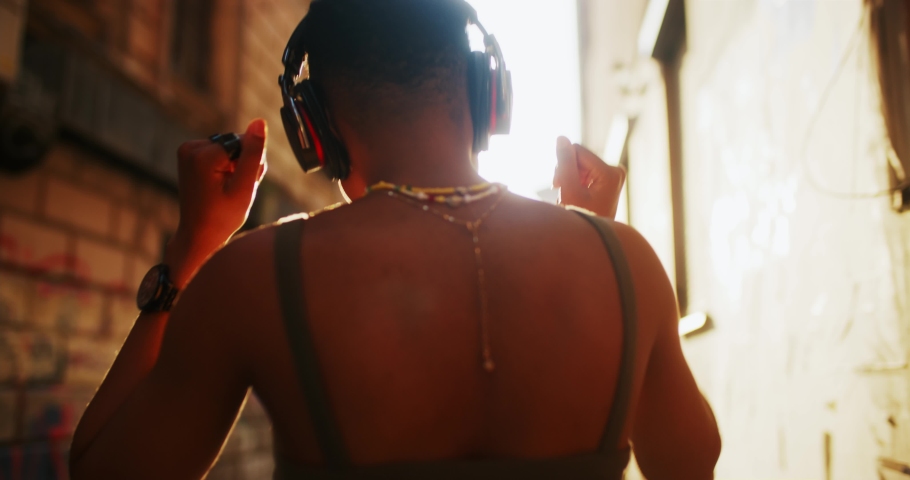 Active cheerful young african woman wearing headphones and listening favorite music outside. Black stylish girl dancing on modern hipster street downtown. Sunny day. People and emotions.