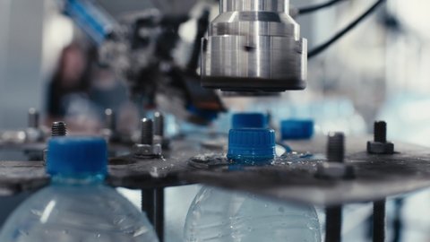 Water factory industrial machine puts caps on plastic PET bottles with water, close up