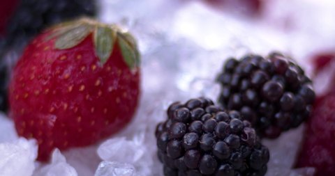 Raspberries, strawberries and blackberries on cold ice. A drop of water falls on the blackberry. Natural cold fruits, juicy and aromatic food.  Slow motion, 8K downscale. 4K.
