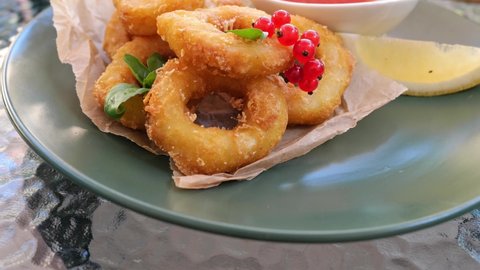 fried squid rings or, golden crispy fried calamari dipped in batter with lemon slice, berries, served with red sauce, restaurant menu appetizer. Fast food