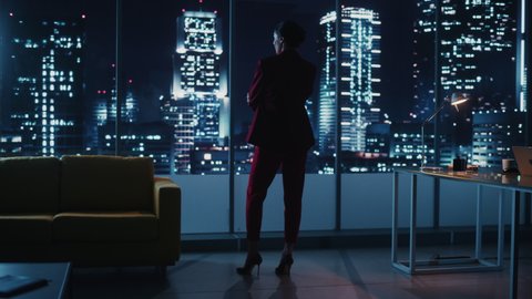 Night Office: Powerful Businesswoman Wearing Stylish Suit Standing and Looking out of the Window on a Big City. Ambitious Successful Female CEO Thinking of Environmental, Social Sides of e-Business