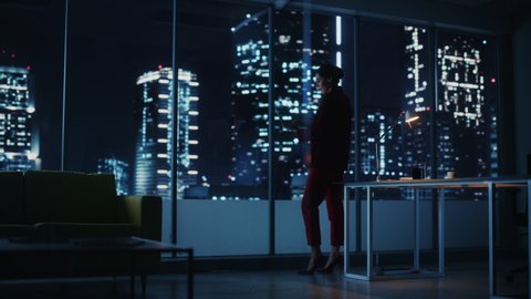 Successful Powerful Businesswoman Wearing Stylish Suit Holding Laptop Standing in Big City Night Office. Female CEO Managing Environmental, Social and Corporate Governance for e-Commerce Empire