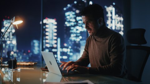 Portrait of Thoughtful Successful Businessman Working on Laptop Computer in His Big City Office at Night. Energetic Digital Entrepreneur does Data Analysis for e-Commerce Strategy. Medium Arc Shot