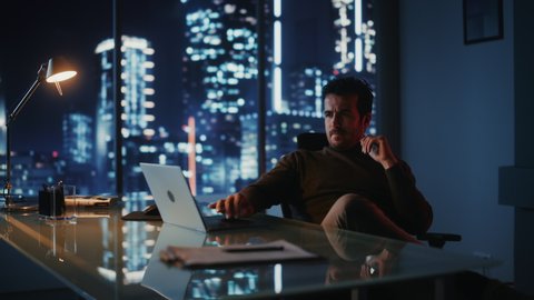 Portrait of Thoughtful Successful Businessman Working on Laptop Computer in His Big City Office at Night. Charismatic Digital Entrepreneur does Data Analysis for e-Commerce Strategy. Arc Medium Shot