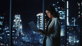 Big City Modern Office at Night: Successful Young Businesswoman Standing and Using Laptop. Beautiful Female Digital Entrepreneur Thinking of Investment Strategy for e-Commerce Project. Medium Shot - Powered by Shutterstock - Get 15% off with code: PIKWIZARD15