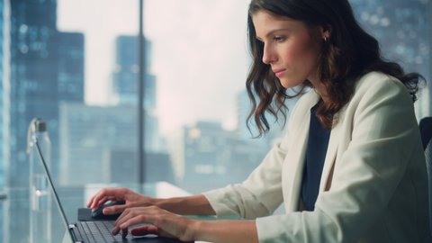 Portrait of Young Successful Caucasian Businesswoman Sitting at Desk Working on Laptop Computer in City Office. Beautiful, Talented Corporate Manager Plan Social Media Strategy for e-Commerce Project