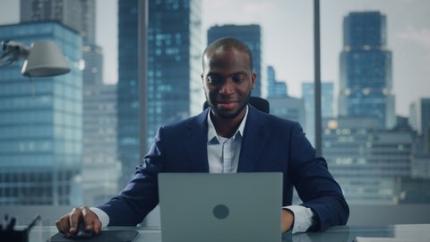Portrait of Successful Black Businessman Working on Laptop Computer in His Big City Office. Professional Digital Entrepreneur does Data Analysis for e-Commerce Strategy assessment. Zoom In Front View