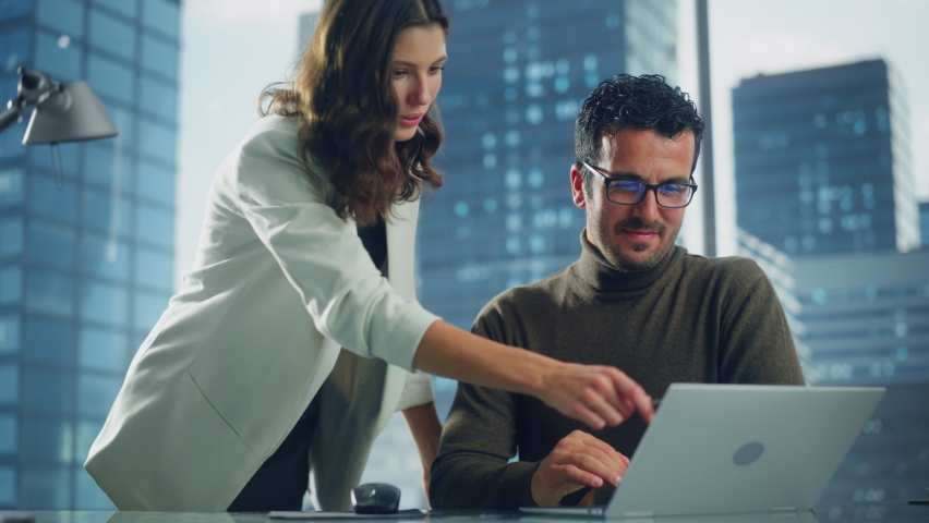 Company CEO and Top Manager Talking, Using Laptop Computer while in Big City Office. Two Successful Professional People Brainstorm, Find Solution to Their e-Commerce Software Investment Strategy