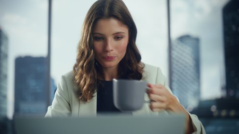 Portrait of Successful Young Businesswoman Sitting at Her Desk Working on Laptop Computer in Big City Office. Beautiful Social Media Strategy Manager Plan Disruptive e-Commerce Campaign