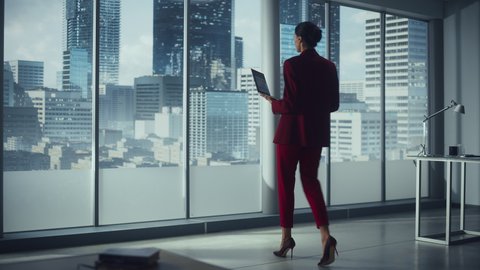 Successful Caucasian Businesswoman Using Laptop While Standing in Office Looking out of Window on Big City. Confident Female Managing Environmental, Social and Corporate Governance