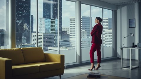 Successful Thoughtful Businesswoman Wearing Perfect Red Suit Standing in Office Looking out of Window on Big City. Confident Female Corporate Top Manager of IT Company Plans Investment Strategy