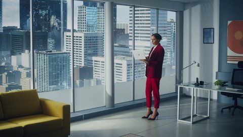 Successful Caucasian Businesswoman Using Laptop While Standing in Office Looking out of Window on Big City. Perfect Confident Female Digital Entrepreneur Developing e-Commerce Software Strategy. Full