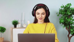 Attractive woman in headphones communicates by video communication using a laptop. A beautiful girl is talking on a webcam with her teacher. Online learning 