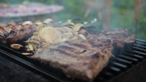 cooking grilled pork ribs with onions. a man's hand turns the ribs with tongs