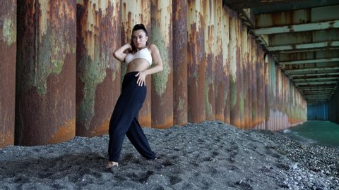 sexy dancehall performance at nature, woman is dancing on sea shore under pier