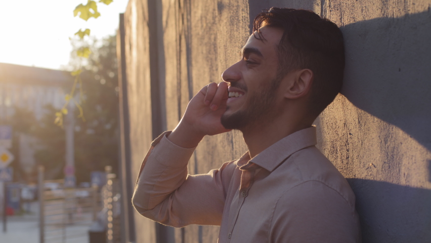 Side view handsome bearded hispanic arabic indian business man client guy standing near stone wall talking on mobile phone answering call talks with smartphone conversation using cellphone in city Royalty-Free Stock Footage #1079143811