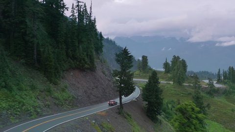 Epic aerial shot car driving with cloudy mountain forest background. Car driving along cinematic winding mountain road. Eco tourism concept, USA 4K footage. Tourists in car exploring National park