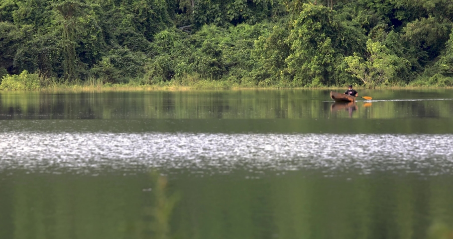 A Man Canoes on a Reflective Lake with a Forest Background in Thailand.