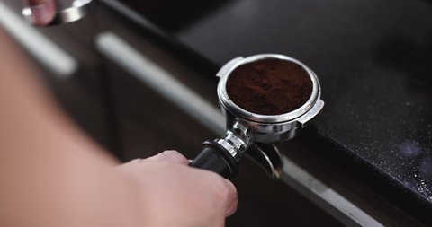 Barista hand holding and pressing tamper on coffee grounds powder in portafilter ready to make cup of coffee.