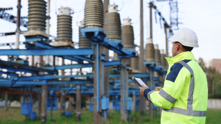 Electrical worker engineer a working with digital tablet, power near tower with electricity. Energy business technology industry concept. Electrical engineer studying reading on tablet. Royalty-Free Stock Footage #1079155658