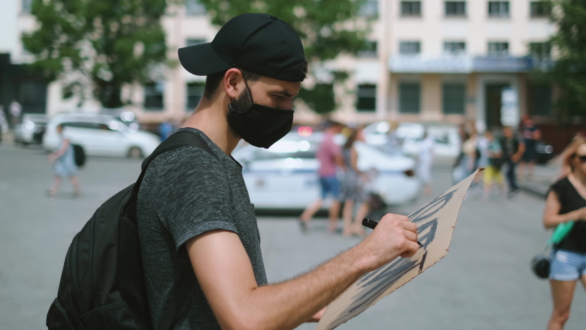 Protester man on rally in covid-19 mask draws sign poster. Rebel on city revolt, resistance strike. Picket activist drawing demonstration banner placard protesting. Royalty-Free Stock Footage #1079156486