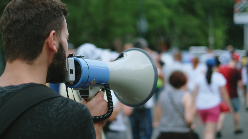 Strike activist demonstrator man on opposition rally riot with megaphone walks. Political protester guy with bullhorn marches in protest crowd. Male rebel speaking on demonstration revolt resistance. Royalty-Free Stock Footage #1079156516