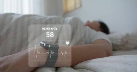 Asia teen woman wear smartwatch for sugar tracker, blood pressure tracking, resting sleep rate on arm IoT tech collect data app device relax body on cozy bed in future life at home.