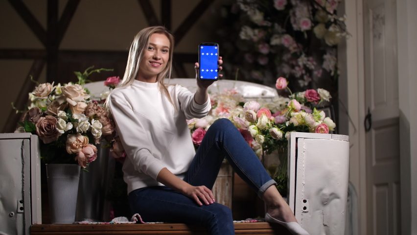 Lady slides swipes chroma key blue screen. Female person holds smart phone device in hands with chromakey. Fit woman on flower background portrait with smiling face looks at camera with blue screens Royalty-Free Stock Footage #1079166128