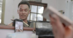 A charming short-haired Asian gay who owns a small beauty salon in the village is writing eyebrows as he uses his mobile phone to record a video to post on social media.