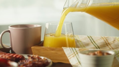 Pouring orange juice in glass close-up. Traditional full English breakfast. National British cuisine, fried eggs with bacon and sausages, fish and chips. American fast food.