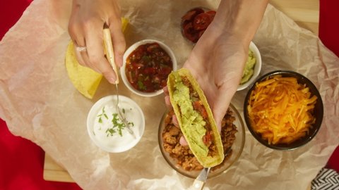 Traditional Mexican food on table, tex mex cuisine. Cooking meat taco, putting sour cream and carrot. Tomato soup with corn and cilantro, guacamole. American dishes top view. Stockvideó