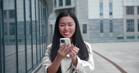 Excited young asian woman rejoices at message on her smartphone. Happy businesswoman looking at cell phone celebrate good news victory success. Portrait of the lucky gambler showing yes winner gesture