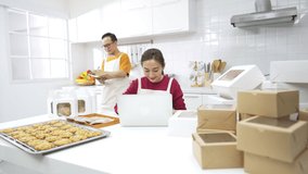 4K Asian couple pastry chef preparing bakery in the kitchen. Male and female bakery shop owner working on laptop computer and mobile phone taking customer order for delivery. Small business concept. - Powered by Shutterstock - Get 15% off with code: PIKWIZARD15