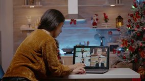Woman talking to business people on video call conference. Adult using remote communication at home while man waiting to celebrate christmas eve festivity together. Work meeting on holiday