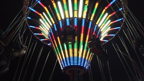 Low angle view of colourful illuminating moving and spinning swing ride or swing carousel on background of night dark sky