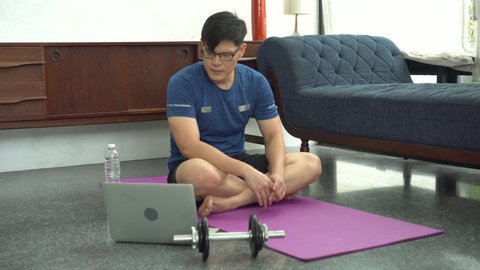 young asian fit man in sportswear doing sit ups and crunch  While watching video training fitness  online tutorials on laptop in living room at home . sport male workout in quarantine