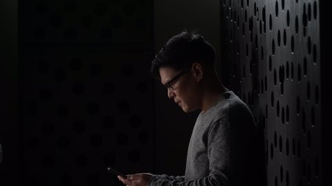 sad young asian man sitting on the floor checking mobile phone with bad news message in the dark at home he lost job in quarantine 