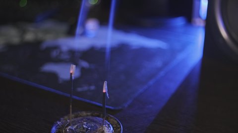 Aroma sticks on the table. Smoldering incense chinese sticks fills the dark room with a smell of frankincense. Just inhale the fragrance and relax. Spreading out smoke in the bluish light.