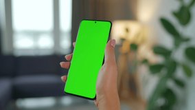 Woman at home using smartphone with green mock-up screen in vertical mode. Girl browsing Internet, watching content, videos. POV.