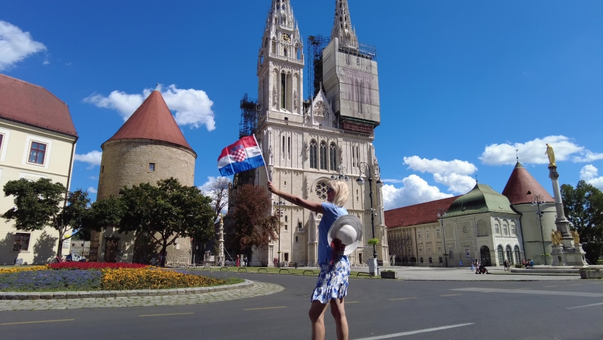 Happy woman with Croatian flag in the square of Zagreb Cathedral of Zagreb city, capital of Croatia in Europe. Colonnade monument of the Assumption of the Blessed Virgin Mary.