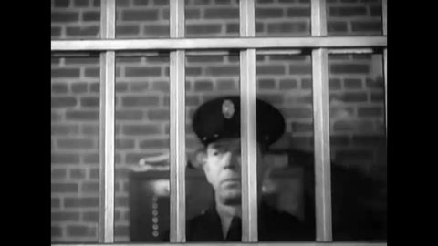 CIRCA 1938 - A prison guard walks up to the bars of a cell.
