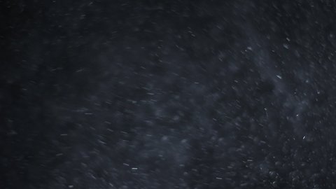 A suspension of white-silver particles in the air on a black background. Some of the particles are blurred in a beautiful bokeh. 4K background for your videos in various mixing modes.
